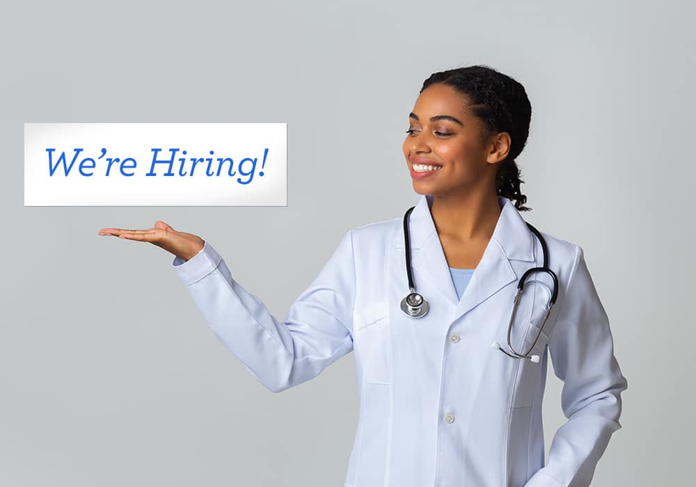 A doctor holding up a now hiring banner.